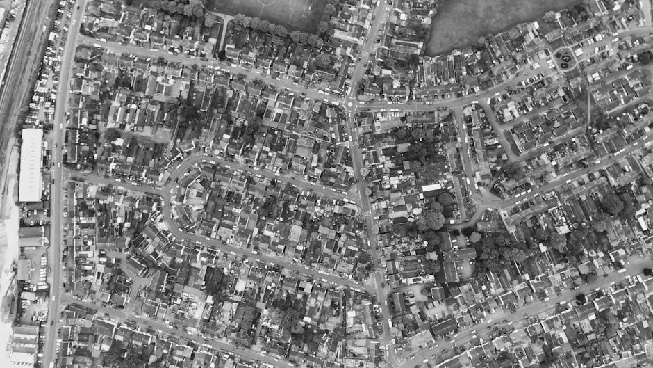 An aerial black-and-white photograph of a densely populated residential area showing a network of narrow streets and closely packed houses with small gardens, driveways, and parked cars along the road